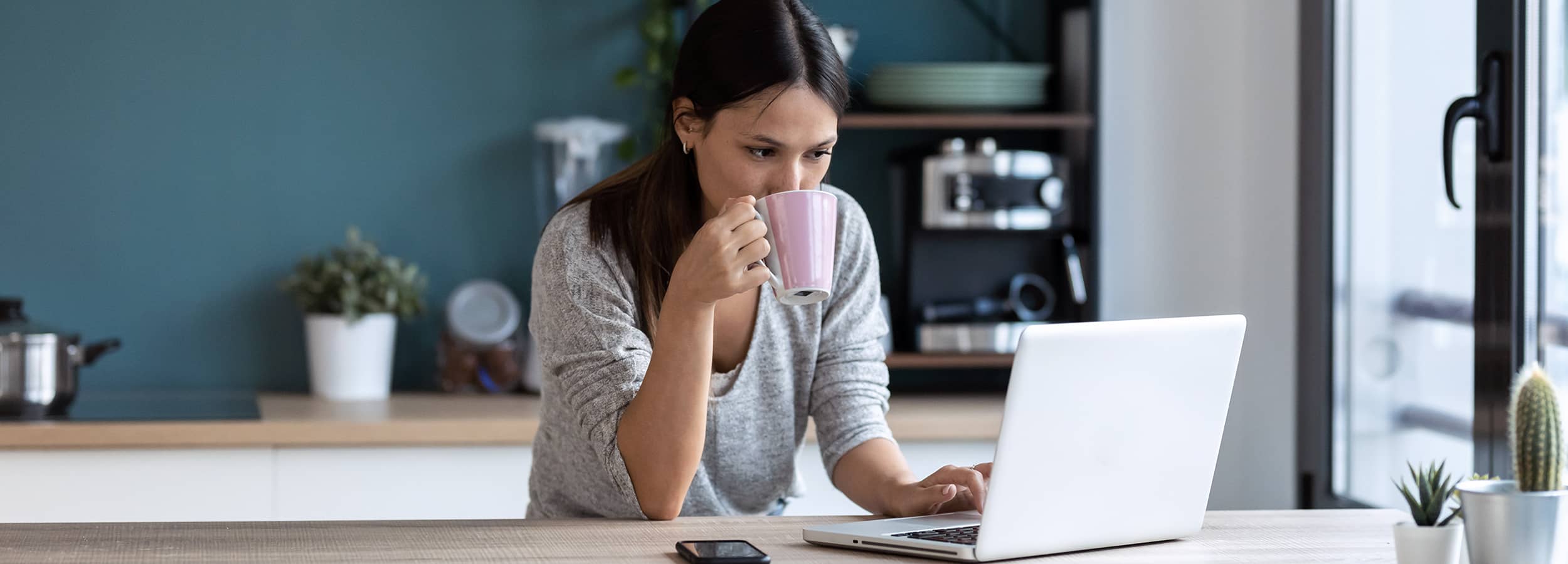 Woman drinking coffee while looking at laptop computer